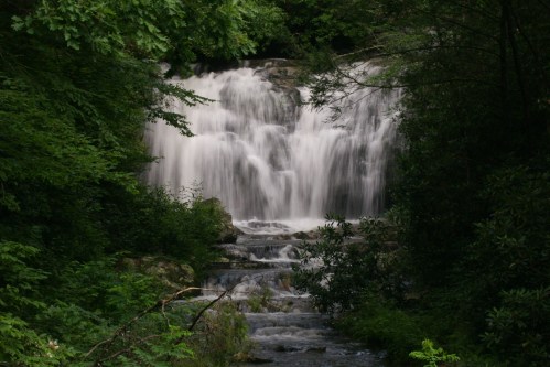 A serene waterfall cascades down rocks, surrounded by lush green foliage and trees.