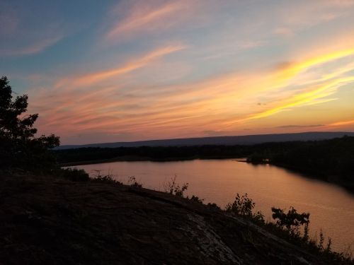 A serene sunset over a river, with colorful clouds reflecting on the water and trees framing the scene.
