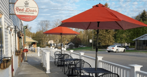 Outdoor seating with red umbrellas at Red Door Coffee House in Lake Ann, MI, on a sunny day.