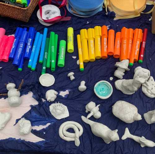 A variety of colorful markers and small clay sculptures arranged on a blue cloth.