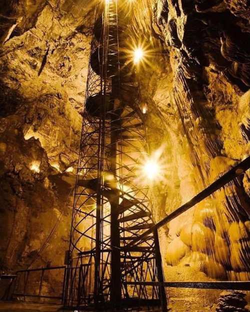 A dimly lit cavern with a tall metal structure and bright lights illuminating the rocky walls.