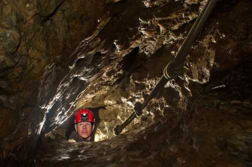 A person in a helmet explores a narrow cave, surrounded by rocky walls and dim lighting.