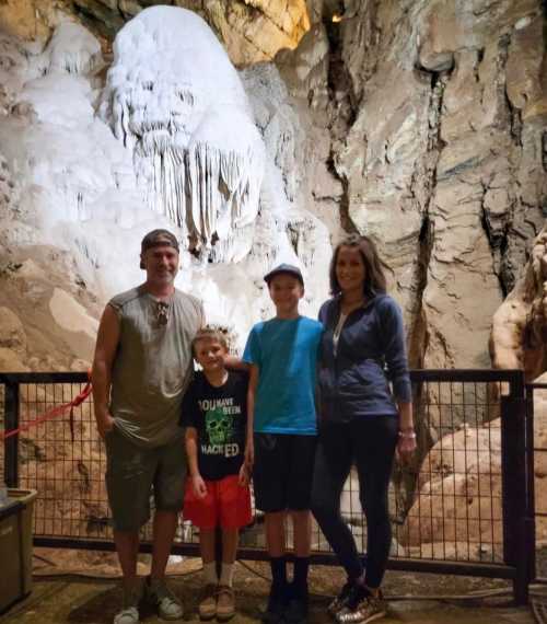 A family of four stands in a cave with rock formations in the background, smiling for the camera.