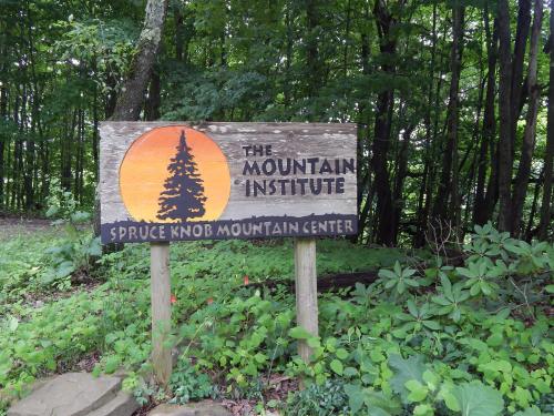 Wooden sign for The Mountain Institute at Spruce Knob Mountain Center, surrounded by greenery and trees.