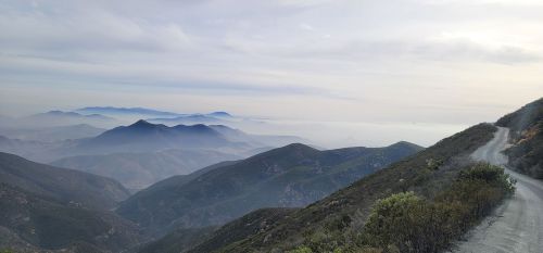 A winding road through misty mountains, with layers of hills fading into the distance under a cloudy sky.