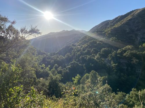 A sunlit landscape with mountains and lush greenery, showcasing a serene natural setting.
