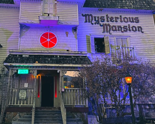 A spooky mansion with a red symbol on the facade, illuminated by colorful lights, and an "Open" sign at the entrance.