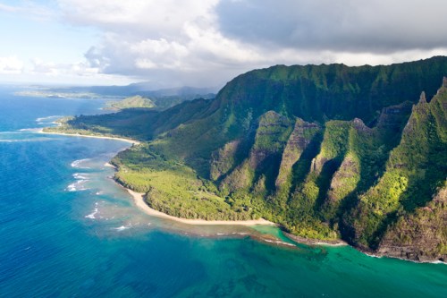 Aerial view of lush green mountains meeting a turquoise ocean, with a sandy beach along the coastline.