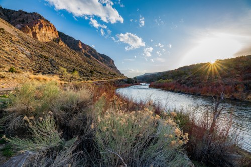 A scenic river flows through a canyon, framed by mountains and bathed in warm sunlight during sunset.