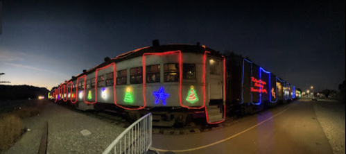 A brightly lit train decorated with colorful holiday lights at dusk, surrounded by a clear sky.