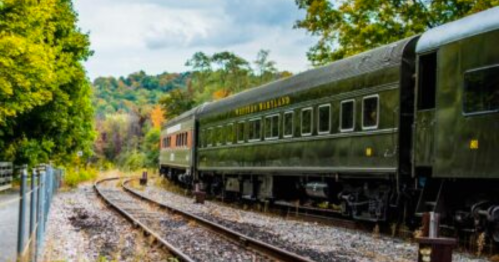 A vintage train car on tracks surrounded by trees and autumn foliage under a cloudy sky.