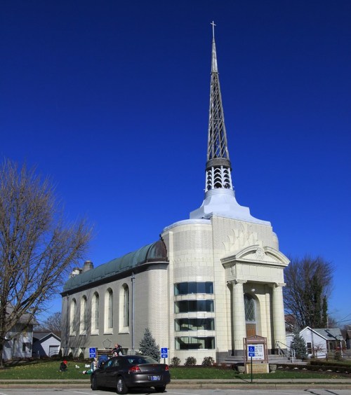 A tall church with a spire against a clear blue sky, featuring a modern design and large windows.