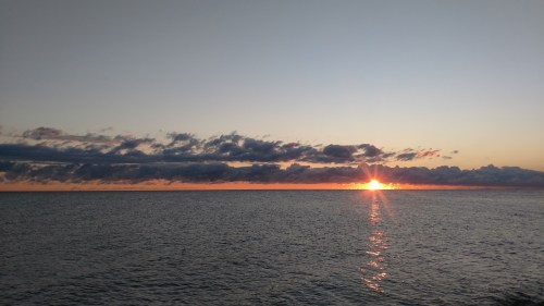 A serene sunset over calm waters, with clouds reflecting warm hues in the sky.