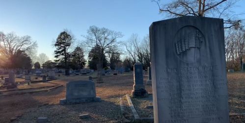 A cemetery at sunset, featuring gravestones and a prominent memorial for John Belton White, a World War Hero.