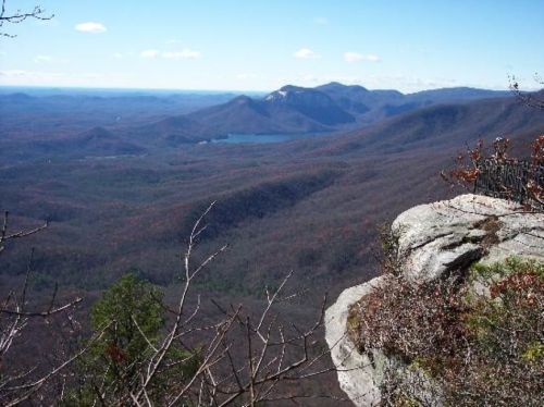 A panoramic view of mountains and valleys under a clear blue sky, with a lake visible in the distance.
