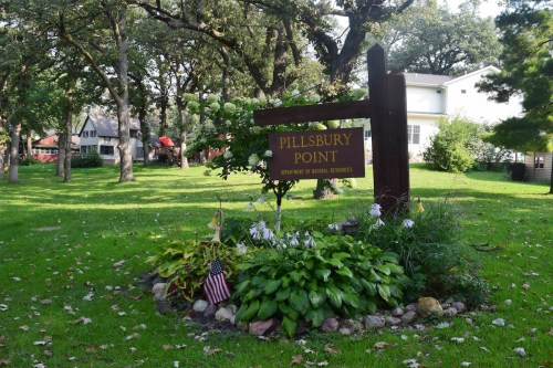 Sign for Pillsbury Point surrounded by greenery and flowers, with houses visible in the background.