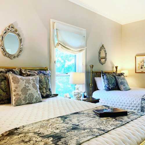 A cozy bedroom with two beds, decorative pillows, mirrors, and soft lighting, creating a warm and inviting atmosphere.