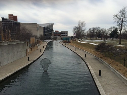 A calm waterway lined with trees and buildings, with a net resting in the water under a cloudy sky.