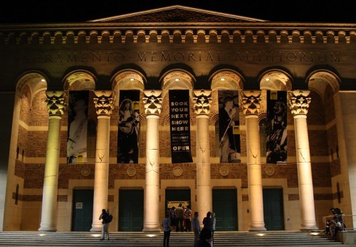 Sacramento Memorial Auditorium at night, featuring grand columns and banners, with people entering the building.
