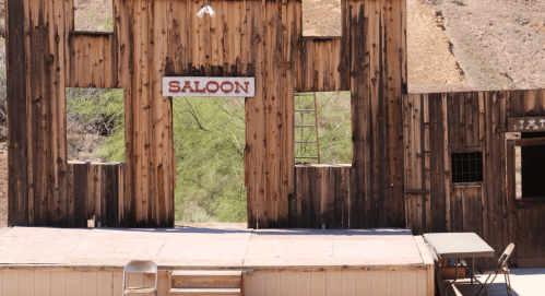 A wooden saloon facade with a sign, featuring empty windows and a stage area in a desert setting.