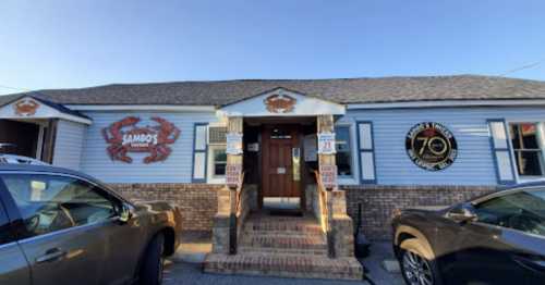 Exterior of Sambo's Tavern, featuring a crab logo, with parked cars in front and a clear blue sky.