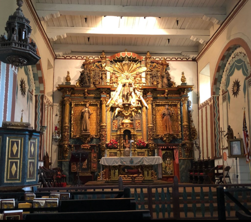 Interior of a historic church featuring an ornate altar with gold details, statues, and decorative elements.