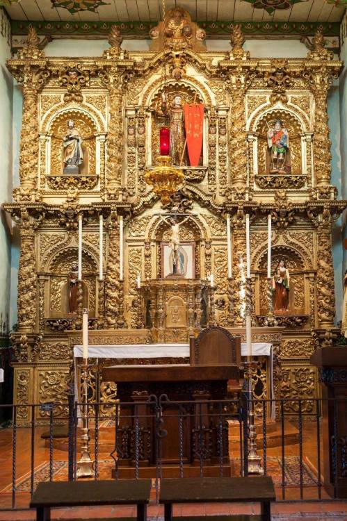 Intricate gold-leaf altar with religious figures, candles, and decorative carvings in a historic church setting.