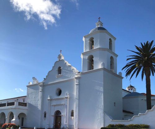 A white church with a bell tower, crosses, and palm trees under a clear blue sky.