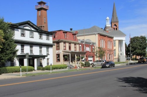 Historic buildings line a street, featuring a mix of architectural styles and a clear blue sky above.