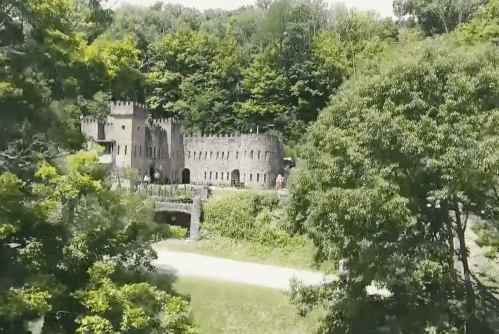 A scenic view of a stone castle surrounded by lush greenery and trees on a sunny day.