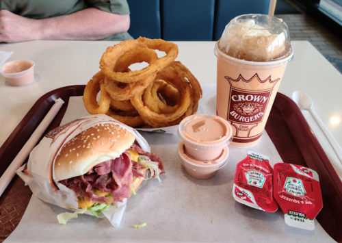 A tray with a burger wrapped in paper, onion rings, a drink, and dipping sauces.