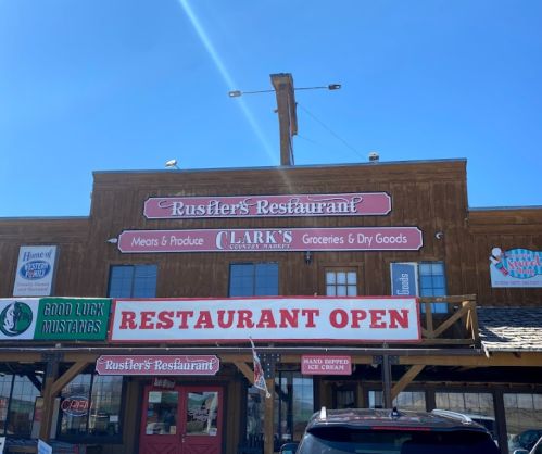 Exterior of Rustler's Restaurant with a sign indicating it's open, featuring a rustic wooden facade and grocery store signage.