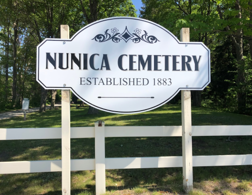 Sign for Nunica Cemetery, established in 1883, surrounded by trees and a white fence.
