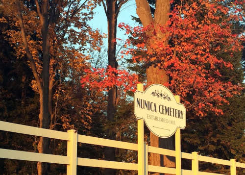 Sign for Nunica Cemetery, established 1883, surrounded by trees with autumn leaves.