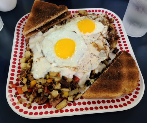 A plate of breakfast featuring two sunny-side-up eggs, hash browns, and toast on a red and white dotted plate.