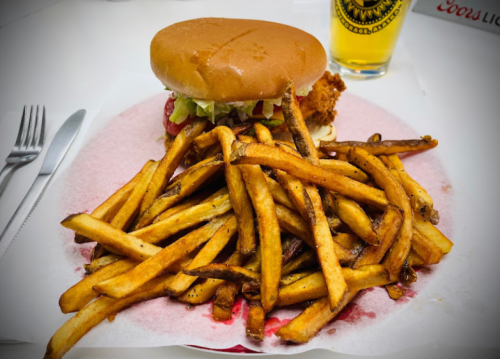 A plate of golden fries with a chicken sandwich topped with lettuce and tomato, alongside a glass of beer.