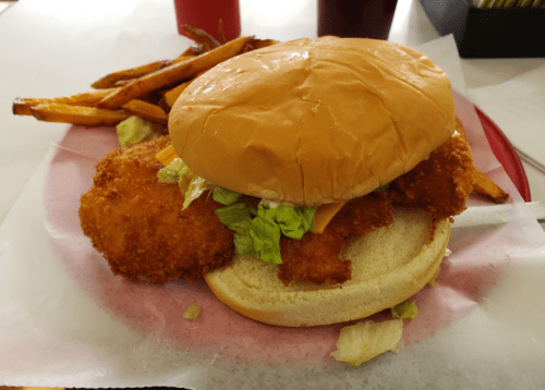 A crispy chicken sandwich with lettuce and cheese, served with a side of golden French fries on a red plate.