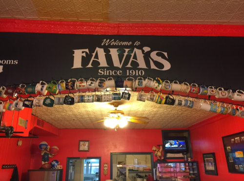 A cozy restaurant interior with a sign reading "Welcome to Fava's Since 1910" and a display of hanging mugs.