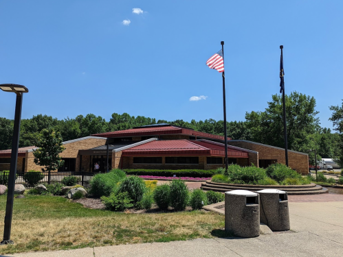 A modern building with a red roof, surrounded by greenery, featuring an American flag and a state flag.