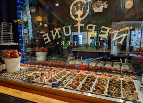 A display of various pastries and desserts in a shop window, with a neon sign reading "Neptune" in the foreground.