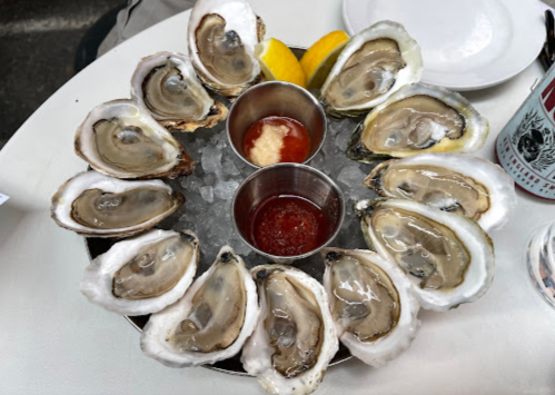 A platter of fresh oysters on the half shell, served with lemon wedges and two dipping sauces.