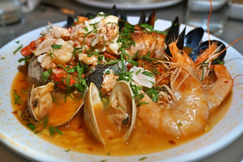 A bowl of seafood stew featuring shrimp, clams, and mussels, garnished with fresh herbs.