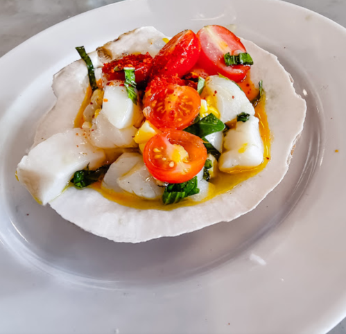 A white plate with a colorful dish featuring diced fish, cherry tomatoes, and herbs in a light sauce.