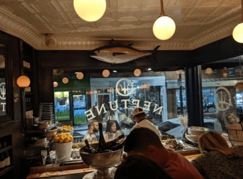 Interior of a seafood restaurant with a large fish mounted on the wall and diners enjoying their meals by the window.