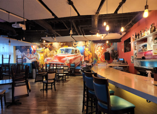 A vibrant bar interior with colorful murals, empty chairs, and a well-lit counter, creating a lively atmosphere.