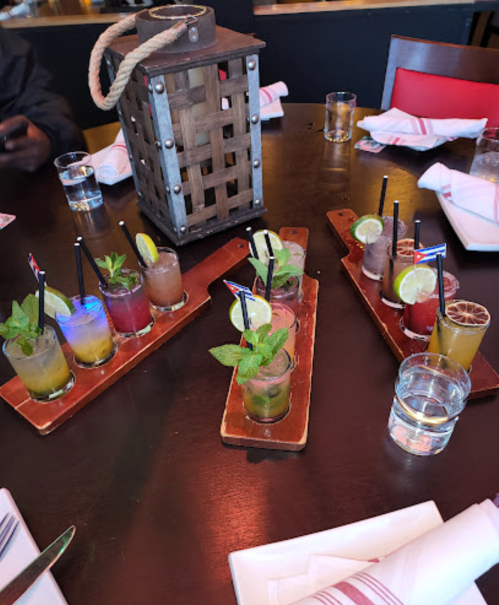 A table with several colorful cocktails garnished with mint and lime, alongside a lantern and glasses of water.