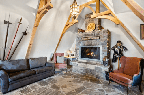 Cozy living room with a stone fireplace, wooden beams, and rustic decor, featuring a sofa and two armchairs.