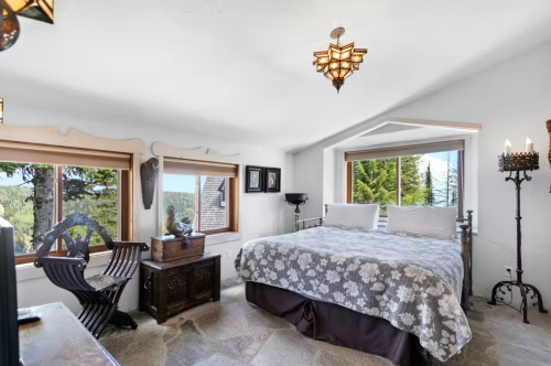 Cozy bedroom with a large bed, decorative windows, and rustic furnishings, surrounded by nature.