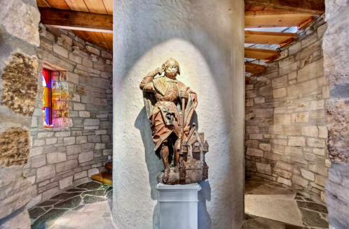 A stone tower interior featuring a statue of a knight on a pedestal, with colorful windows and rustic stone walls.