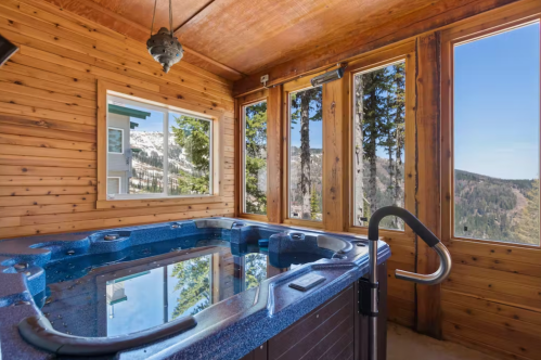 A cozy indoor hot tub with large windows showcasing a mountain view and wooden walls.
